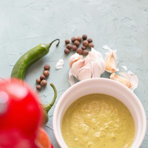 Green curry sauce with spices and garlic on a textured surface, showcasing vibrant culinary elements.