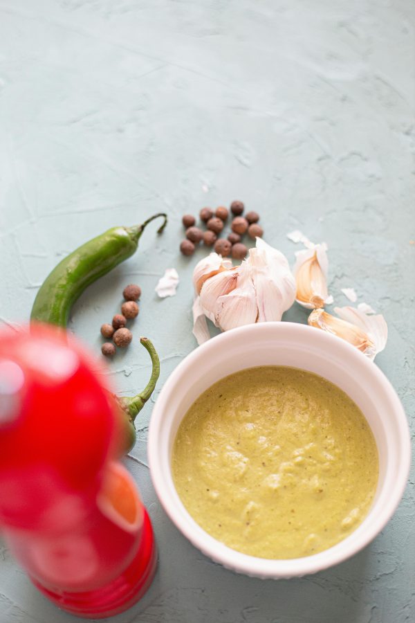 Green curry sauce with spices and garlic on a textured surface, showcasing vibrant culinary elements.